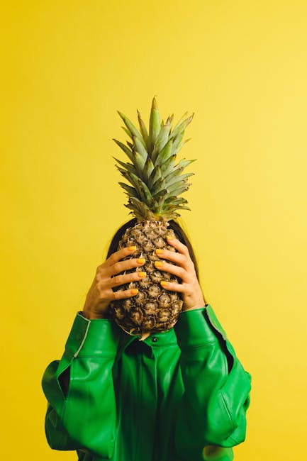 A person peeling a pineapple with a sharp knife, yellow flesh exposed
