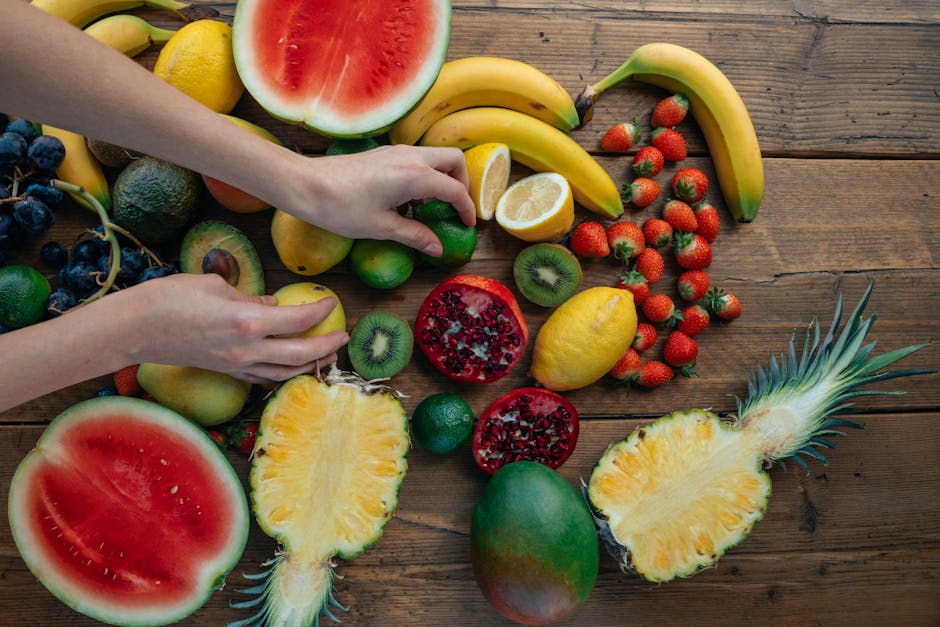 A person's hand gently pressing the top of a pineapple to check for ripeness, surrounded by other fresh fruits
